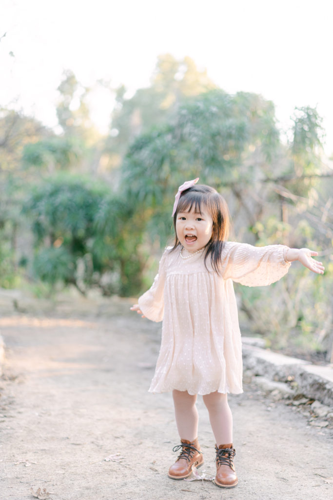 toddler girl wearing blush pink dress at park with lots of greens