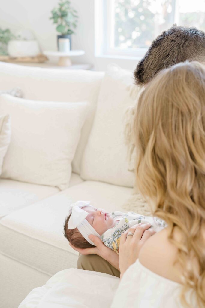 parents posing with newborn baby on white linen couch at their san diego home