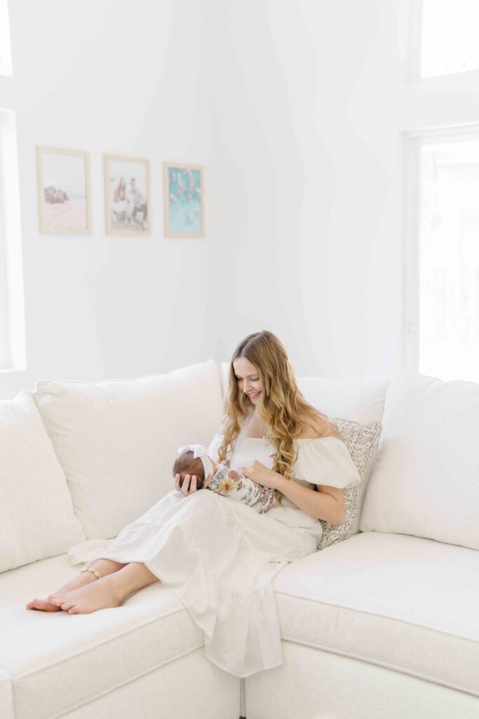 lifestyle newborn photography in san diego of mom and baby sitting on white linen couch